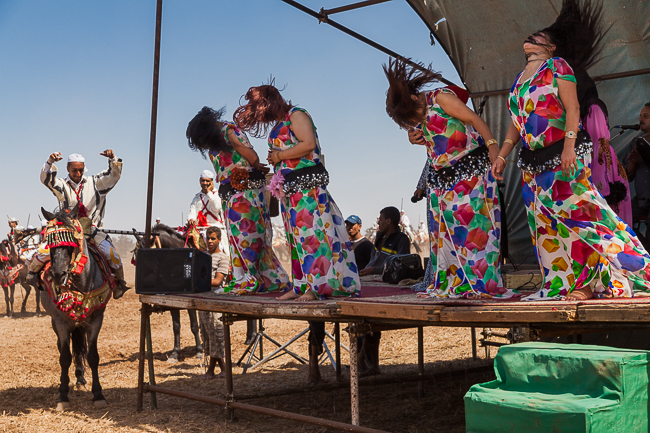 Chikhates perform music and dance as a rider approaches the stage on horseback during a Moroccan moussem.