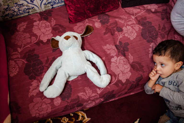 A young boy stands beside a stuffed toy on a floral bedspread in the room he shares with his mother in Casablanca.