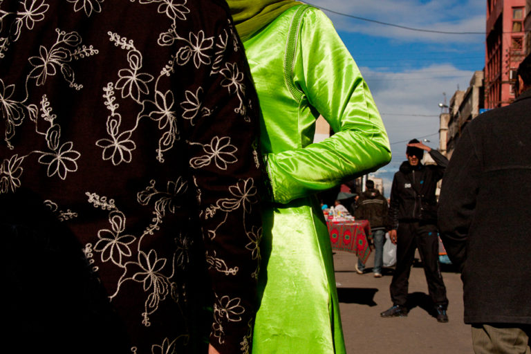 Deux personnes vues de dos portent des vêtements noir fleuri et vert vif dans une rue de Casablanca.